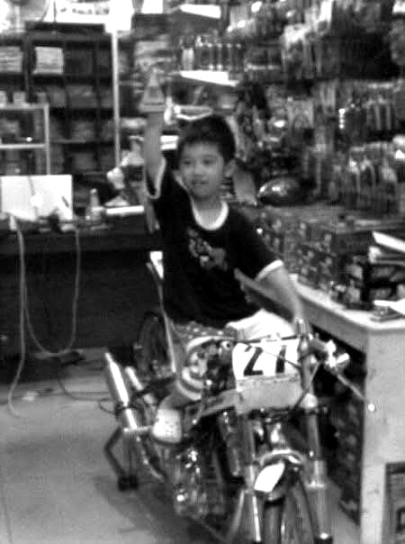 Seorang anak duduk di atas motor balap di dalam toko
